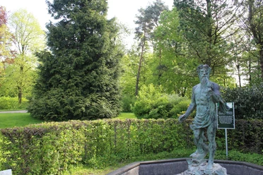 Neptunstatue im Park, umgeben von üppigem Grün und Bäumen, ein Hinweis auf kulturellen Reichtum.