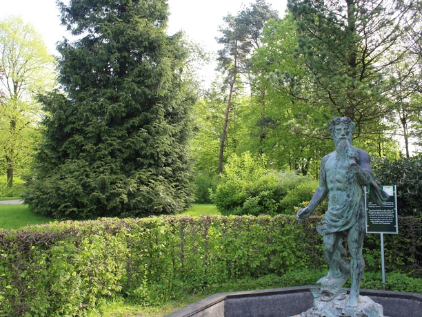 Neptunstatue im Park, umgeben von üppigem Grün und Bäumen, ein Hinweis auf kulturellen Reichtum.