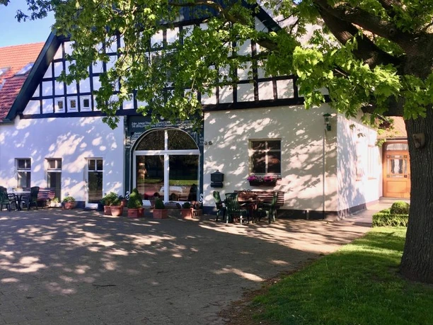 Ein traditionelles Fachwerkhaus mit strahlender weißer Fassade unter einer großen, grünen Eiche.