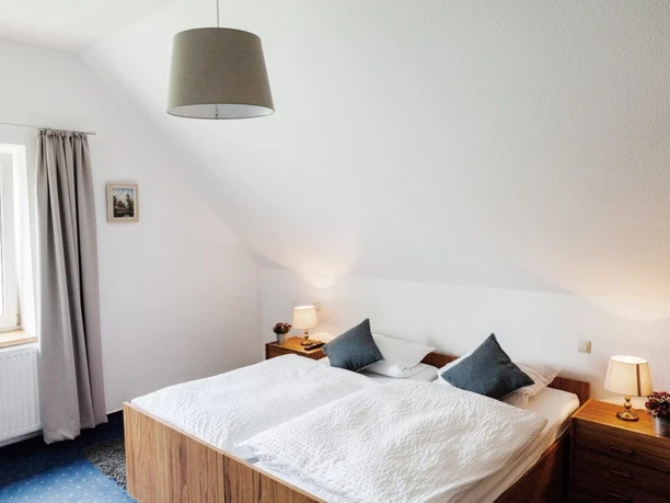 Helles Schlafzimmer mit Dachschräge, Doppelbett und Nachttischen, sanft beleuchtet durch kleine Lampen.