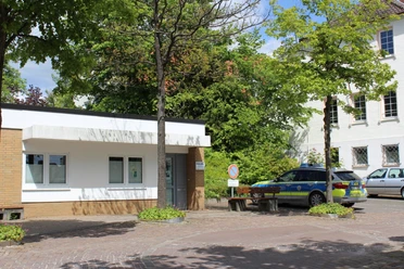 Polizeistation Polizeistation mit kleinem, flachem Gebäude und polizeilichen Einsatzfahrzeugen, umgeben von Bäumen.