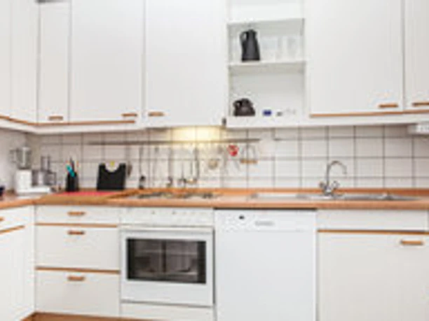 Moderne weiße Einbauküche mit Herd, Spüle und Geschirrspüler; schlichte Arbeitsfläche mit Holzakzenten.