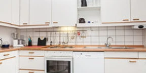 Ferienwohnung Berger 4.jpg Moderne weiße Einbauküche mit Herd, Spüle und Geschirrspüler; schlichte Arbeitsfläche mit Holzakzenten.