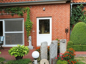 Ferienwohnung an der Kirche Ferienwohnung aus rotem Backstein mit begrüntem Eingangsbereich und bunten Blumengestecken.