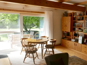 Wohnzimmer Ein helles Wohnzimmer mit Holzboden, Esstisch und Stühlen aus Holz vor großen Fenstern.