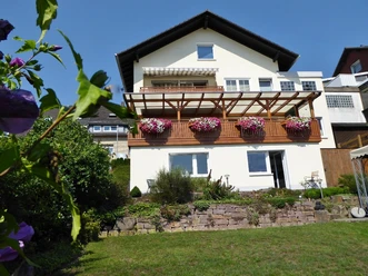 Ansicht.JPG Weißes Haus mit Balkon aus Holz und bunt blühenden Blumen, gepflegter Garten im Vordergrund