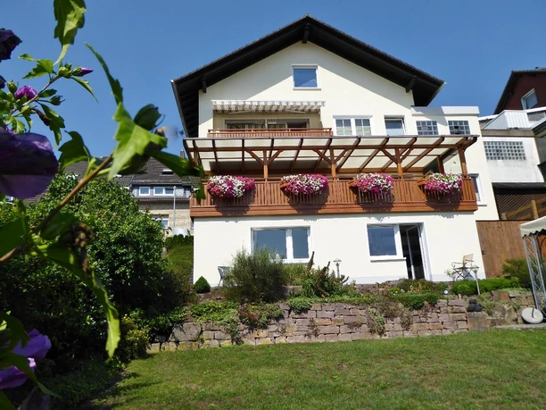 Ansicht.JPG Weißes Haus mit Balkon aus Holz und bunt blühenden Blumen, gepflegter Garten im Vordergrund