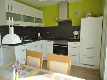 Moderne Küche in Weiß mit Hängeschränken, Einbaugeräte, Esstisch und Holzstühle.