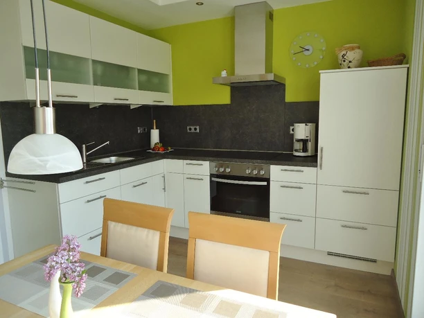 Moderne Küche in Weiß mit Hängeschränken, Einbaugeräte, Esstisch und Holzstühle.