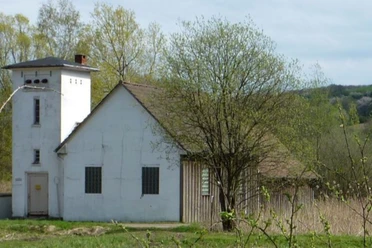 Weißes Pumpenhaus mit Turm, umgeben von Bäumen, auf einer Wiese im ländlichen Gebiet Oberösterreichs.