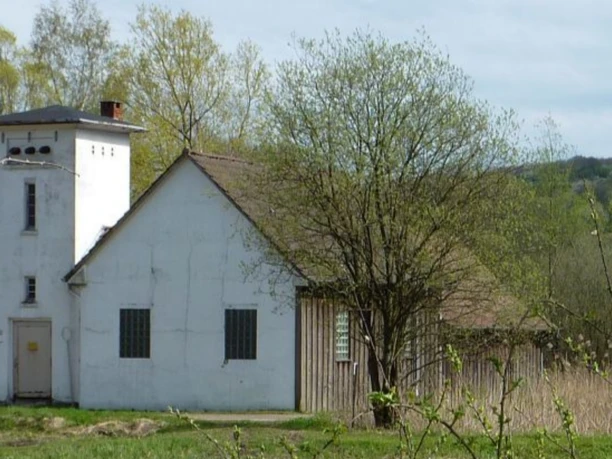 Weißes Pumpenhaus mit Turm, umgeben von Bäumen, auf einer Wiese im ländlichen Gebiet Oberösterreichs.