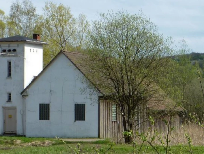 Weißes Pumpenhaus mit Turm, umgeben von Bäumen, auf einer Wiese im ländlichen Gebiet Oberösterreichs.