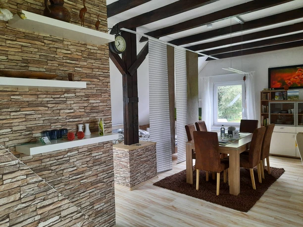 fewo-eggetal-1.jpg Offener Essbereich mit Holzbalken und Natursteinakzentwand, stilvoll eingerichtet, helles Tageslicht.