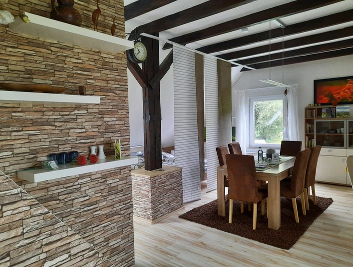 fewo-eggetal-1.jpg Offener Essbereich mit Holzbalken und Natursteinakzentwand, stilvoll eingerichtet, helles Tageslicht.