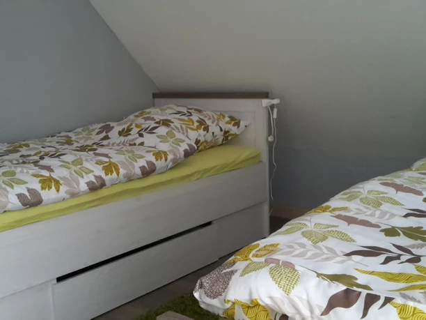 fewo-eggetal-4.jpg Zwei Betten mit floral bedruckten Decken in einem hellgrau gestrichenen Schlafzimmer unter Schrägdach.