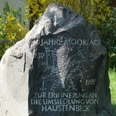 Gedenkstein mit eingravierter Landkarte und der Aufschrift "50 Jahre Moorlage" zwischen Pflanzen.
