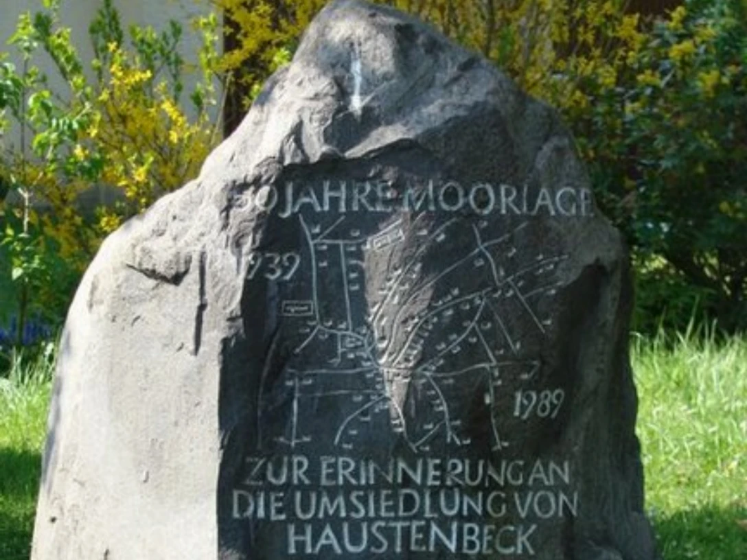 Siedlung Moorlage Gedenkstein mit eingravierter Landkarte und der Aufschrift "50 Jahre Moorlage" zwischen Pflanzen.