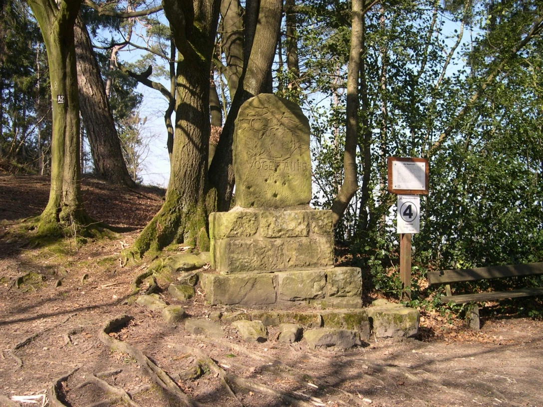 Steinmonument umgeben von Bäumen mit einer Tafel und Wegweiser, Standort Vogeltaufe.