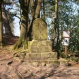 Vogeltaufe Steinmonument umgeben von Bäumen mit einer Tafel und Wegweiser, Standort Vogeltaufe.