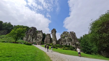 Externsteine Steinerne Felsformationen inmitten einer grünen Wiese, von Besuchern auf einem Kiesweg erkundet.