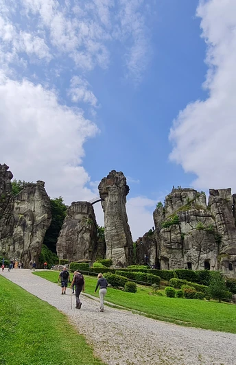 Externsteine Steinerne Felsformationen inmitten einer grünen Wiese, von Besuchern auf einem Kiesweg erkundet.