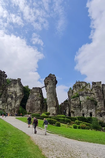 Externsteine Steinerne Felsformationen inmitten einer grünen Wiese, von Besuchern auf einem Kiesweg erkundet.