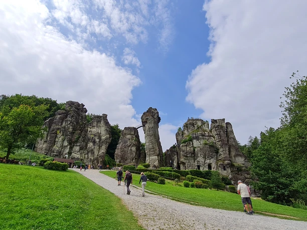 Externsteine Steinerne Felsformationen inmitten einer grünen Wiese, von Besuchern auf einem Kiesweg erkundet.