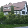 wiehen-inn-1.jpg Fachwerkhaus mit rotem Ziegeldach, umgeben von grünen Bäumen und Hecken an einer ruhigen Straße.