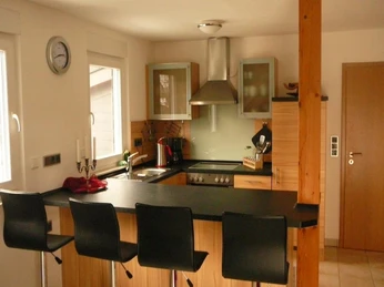 Rahe-2.jpg Moderne Küche mit Insel und Barhockern, ausgestattet mit Edelstahlgeräten und Holzfronten.