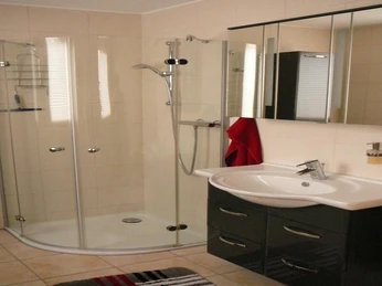 Rahe-4.jpg Ein modernes Badezimmer mit Eckdusche, Waschbecken mit schwarzer Kommode und einem rot-gestreiften Teppich.