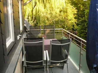Rahe-3.jpg Balkon mit Tisch und vier Stühlen, umgeben von üppigem Grün. Eine ruhige Oase neben einem Haus.