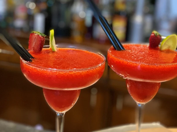 Zwei leuchtend rote Erdbeer-Cocktails in eleganten Gläsern, verziert mit Limette und Erdbeere.