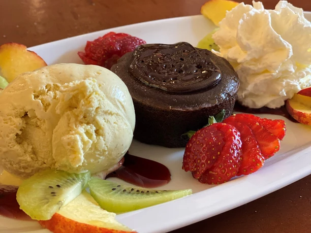 Ein Dessertteller mit Schokoladenkuchen, Vanilleeis, Sahne und frischen Früchten wie Erdbeeren und Kiwi.