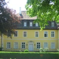 Bökerhof Historisches gelbes Herrenhaus mit weißen Fensterrahmen, umgeben von üppigem Grün und Bäumen.