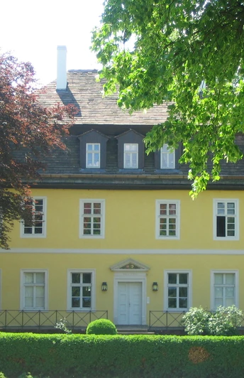 Bökerhof Historisches gelbes Herrenhaus mit weißen Fensterrahmen, umgeben von üppigem Grün und Bäumen.