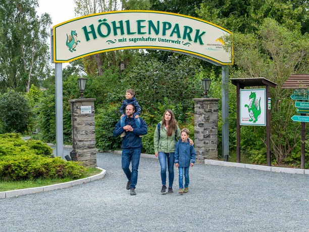 Entrance area of the cave park with family and signposts in green surroundings.