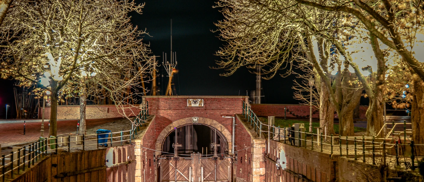 Greetsiel in Abendstimmung Beleuchtete Schleuse in Greetsiel, umgeben von kahlen Bäumen, spiegelt sich im ruhigen Wasser der Nacht.
