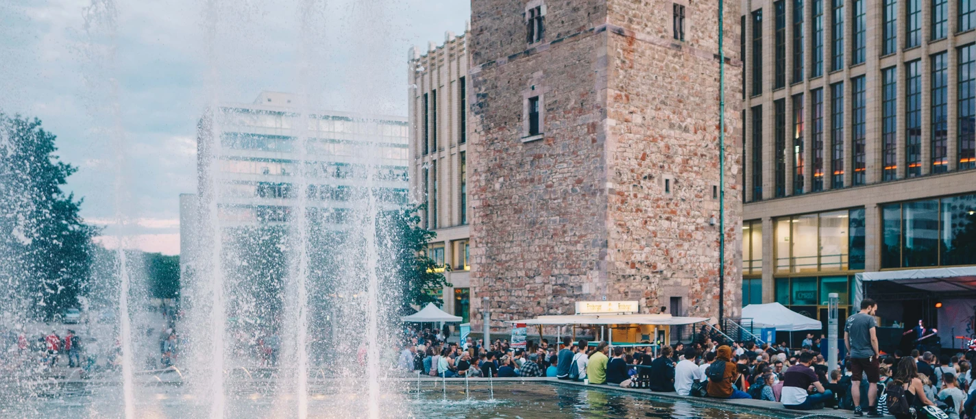 fete_09129_ernestouhlmann.jpg Ein hoher Backsteinturm am Abend, umgeben von springenden Wasserfontänen und Menschenmengen.