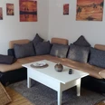FeWo_Büsse_4.jpg Gemütliches Wohnzimmer mit beiger Couch, weißen Kaffeetisch und Wandbildern in warmen Tönen.