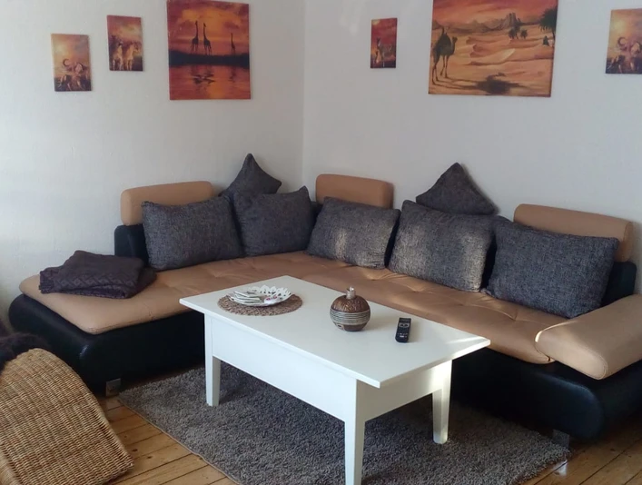 FeWo_Büsse_4.jpg Gemütliches Wohnzimmer mit beiger Couch, weißen Kaffeetisch und Wandbildern in warmen Tönen.