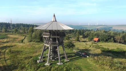 Eggeturm Holzturm auf grüner Wiese mit Sicht auf sanfte Hügel im Hintergrund, vermittelt Naturverbundenheit.
