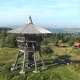 Eggeturm Holzturm auf grüner Wiese mit Sicht auf sanfte Hügel im Hintergrund, vermittelt Naturverbundenheit.