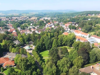 Luftaufnahme eines historischen Kurparks mit umliegenden Gebäuden und Hügeln im Hintergrund.