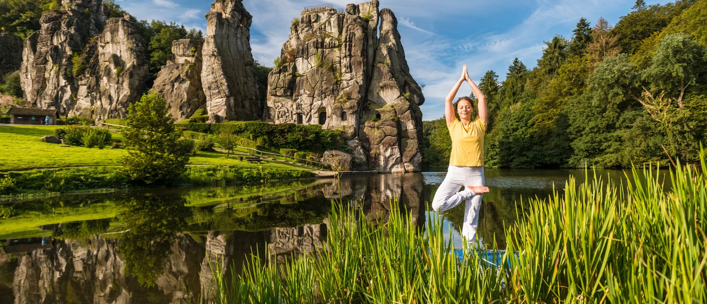 Eine Person beim Yoga im freien, grünen Umfeld vor den beeindruckenden Externsteinen.