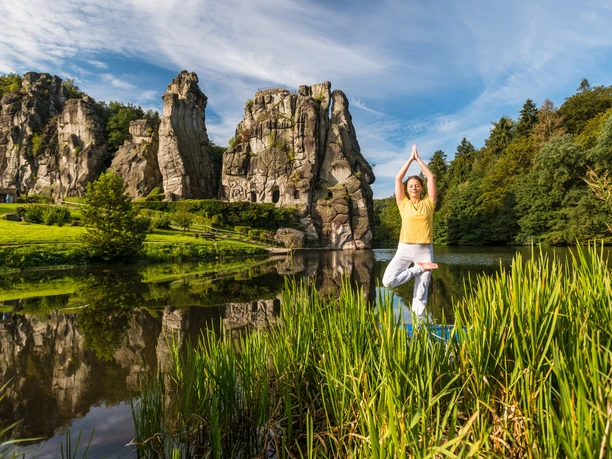 Yoga an den Externsteinen Eine Person beim Yoga im freien, grünen Umfeld vor den beeindruckenden Externsteinen.