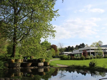 Bad Meinberger Badehaus Das Bad Meinberger Badehaus umgeben von Grünflächen, Bäumen und einem Teich bei sonnigem Wetter.