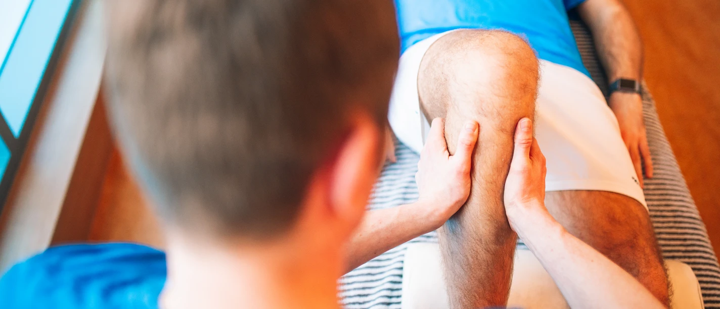 Physiotherapie Ein Physiotherapeut behandelt ein Knie, indem er es mit beiden Händen stützt und bewegt.