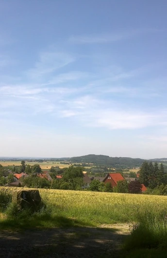 Weitläufige Landschaft mit Feldern und Hügeln, im Vordergrund ein Dorf mit traditionellen Häusern.