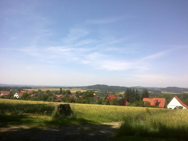 Schöne Aussicht Weitläufige Landschaft mit Feldern und Hügeln, im Vordergrund ein Dorf mit traditionellen Häusern.