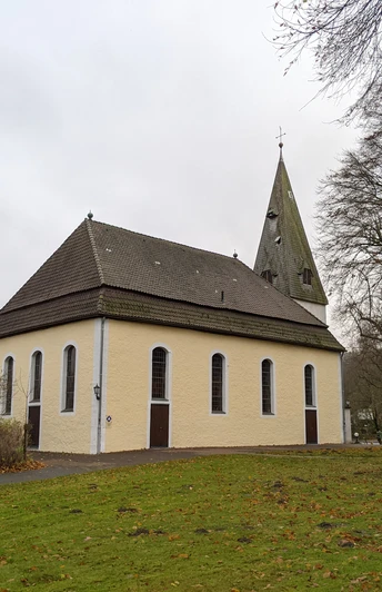 Kirche Stapelage_2©Tourist-Information Lage.jpg Die Kirche Stapelage mit spitzem Turm, umgeben von Bäumen und Rasen, unter bedecktem Himmel.